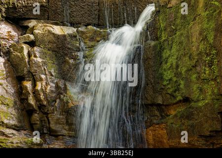 Eine Wasserkaskade, die über Sandsteinfelsen einer kleinen Klippe bei Plunge Mill in der Nähe von Edenfield, Rossendale, Lancashire fließt. Stockfoto