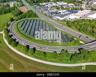 Luftdrohnenfoto einer großen Reihe von Photovoltaik-Solarpaneelen neben einer Autobahnzufahrt Stockfoto