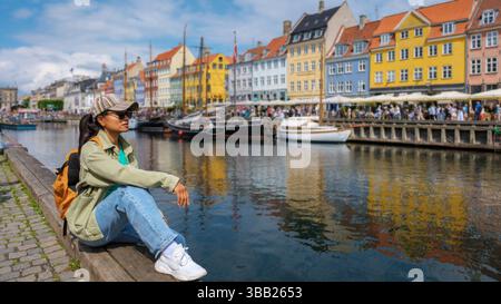 Aian-Frauen besuchen Nyhavn, Kopenhagen, Dänemark, umgeben von bezaubernden Gebäuden und Booten, die sich auf dem ruhigen Wasser spiegeln. Die perfekte Mischung aus Kultur und Natur am Mittag. Stockfoto