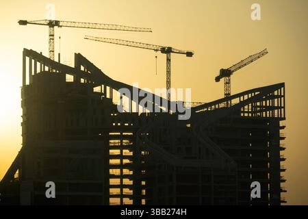 Bau eines neuen Gebäudes. Viele Hochhauskrane und industrielle Baumaschinen gegen die Sonne. Silhouettenkrane Gebäude Stockfoto