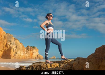 Sportliche Frau, die auf Felsen steht und die Hände auf den Hüften hat, genießt die Aussicht Stockfoto
