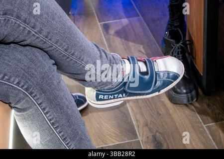 Nahaufnahme von ausgeliehenen Bowlingschuhen, die über Jeans auf Holzboden getragen wurden Stockfoto