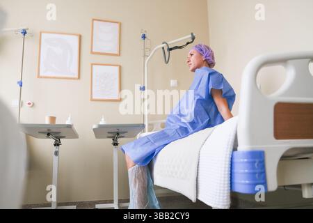 moskau, russland, 19.02.2025 Eine Frau in einem Krankenhausbett mit einem lila Hut auf. Sie trägt ein blaues Kleid und hat ihre Beine gestützt Stockfoto