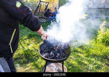 moskau, russland, 10.05.2025 Eine Person kocht auf einem Grill im Garten. Der Rauch vom Grill steigt in die Luft Stockfoto
