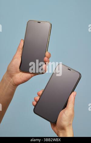 Frau, die zwei Smartphones mit leeren Bildschirmen auf blauem Hintergrund hält Stockfoto