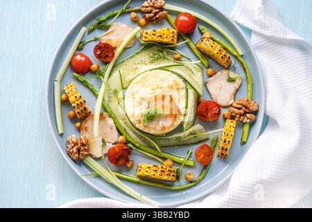 Bowell mit Couscous, Gurke, Tomaten, Spargel und Mais, mit Hähnchenstücken auf einem hellblauen Teller mit einer weißen Serviette. Blick von oben. Kopierraum. Stockfoto