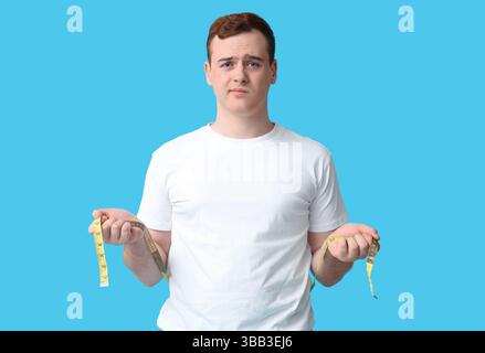 Junger übergewichtiger Mann mit Maßband auf blauem Hintergrund. Gewichtszunahme-Konzept Stockfoto