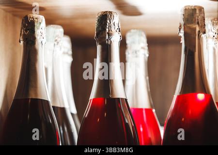 Nahaufnahme von Sektflaschen mit Rosenwein auf Holzregal im Umgebungslicht Stockfoto