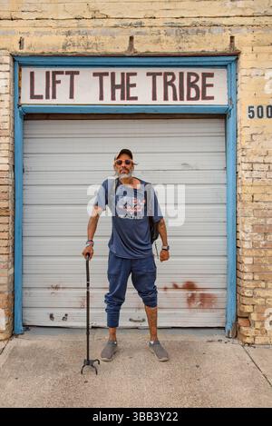 Mann mit Stock, der vor dem Garagentor in einem gelben Backsteingebäude steht, mit Worten, hebe den Stamm darüber. Stockfoto
