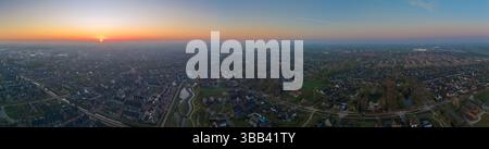 Ein Panoramablick auf den Sonnenaufgang über Nijkerk mit einer ruhigen Wohngegend mit gewundenen Straßen und einem glitzernden Fluss, der das Morgenlicht reflektiert. Stockfoto