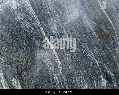 Nahaufnahme einer dunklen Gesteinsoberfläche mit weißen und gelben Streifen. Stockfoto