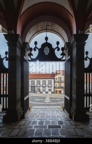 Majestätischer bogenförmiger Eingang der Kathedrale von Angra do Heroismo mit kunstvollen schmiedeeisernen Toren, die den Blick auf den kopfsteingepflasterten platz im Freien einrahmen. Historisch Stockfoto