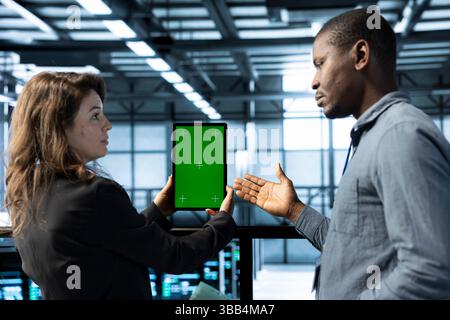 Team von Server-Hub-Ingenieuren, die einen Green-Screen-Laptop verwenden und Sicherheitsprüfungen durchführen. IT-Spezialisten für Rechenzentren überprüfen Firewall-Regeln auf Modellgeräten, protokollieren Vorfalldetails und sprechen Stockfoto