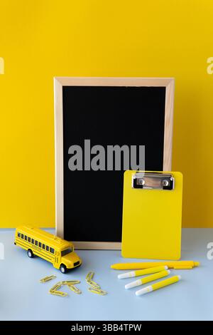 Gelbes Schulmotiv mit Clipboard-Markierungen, Büroklammern und Spielzeugbus in einem klaren, minimalistischen Layout, das an die Schulstimmung erinnert Stockfoto