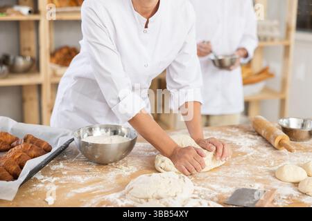 Niedliche Teige auf dem Tisch in der Bäckerei mit Nahaufnahme von Frauenhänden, die gekonnt Teig an der Lebensmittelproduktionslinie kneten Stockfoto
