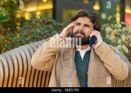 Indischer junger Geschäftsmann Tourist mit schlechten stressigen Nachrichten, die per Smartphone anrufen. Traurig frustrierter verwirrter libanesischer bärtiger Kerl hat Probleme mit unangenehmen Ferngesprächen in der Innenstadt Stockfoto