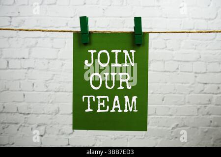Schließe dich unserem Team-Text an, der auf einer Papierkarte mit Seil auf weißem Backstein hängt Stockfoto