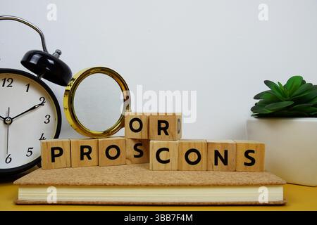 Lupe und Wecker mit Holzblöcken Buchstaben PRO ODER CONS Textnachricht auf gelbem Hintergrund Stockfoto