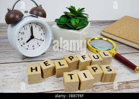 Lupe und Wecker mit Holzblöcken Alphabet Buchstaben HILFREICHE TIPPS Textnachricht auf hölzernem Hintergrund Stockfoto