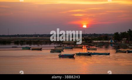 Der atemberaubende Sonnenuntergang beleuchtet den Hafen in Mannar, Sri Lanka. Farbenfrohe Fischerboote, die sanft auf dem goldenen Wasser schwimmen. Stockfoto