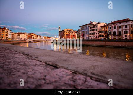 Urbane Szene bei Sonnenuntergang im Stadtzentrum von Pisa. Die Lungarni glänzen sanft an einem typischen Frühlingsabend. Stockfoto