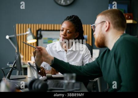 Kollegen, die ein Projekt im modernen Büro diskutieren, eine afroamerikanische Frau und ein kaukasischer Mann, die ein Tablet-Gerät verwenden, Ideen und Kollabo sammeln Stockfoto