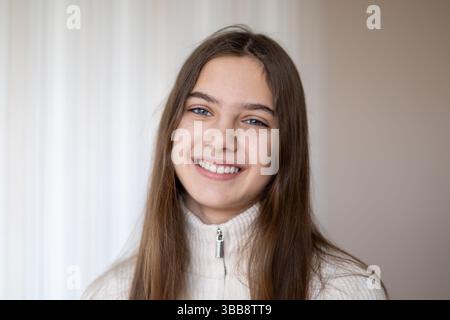Lächelnde junge Frau in lässigem Pullover. Porträt einer fröhlichen jungen Frau mit langen Haaren, die einen leichten Pullover trägt und natürlich gegen ein weiches lächelt Stockfoto