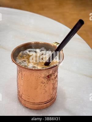 Gekühlter Eiskaffee mit Strohhalm in einer Metalltasse. Auf dem weißen Marmortisch. Stockfoto
