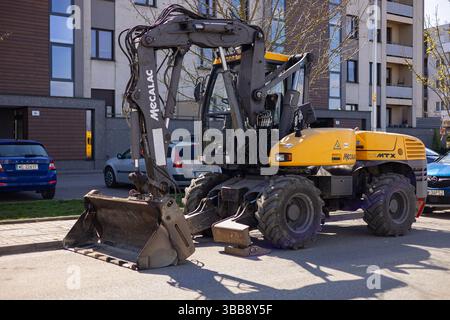 Wroclaw, Polen-8. April 2025: Schwerer Baggerlader parkt an sonnigem Tag auf der Stadtstraße in der Nähe eines Wohngebäudes. Stockfoto