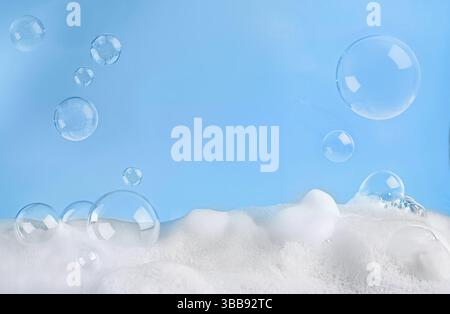 Flauschiger weißer Seifenschaum und Luftblasen, die anmutig über ihm auf blauem Hintergrund schweben Stockfoto