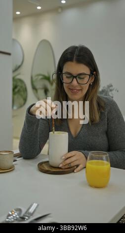 Frau genießt Kaffee drinnen in einem modernen Luxusrestaurant mit heller Beleuchtung, stilvoller Einrichtung und entspannter Atmosphäre und schlürft ruhig ein Getränk Stockfoto
