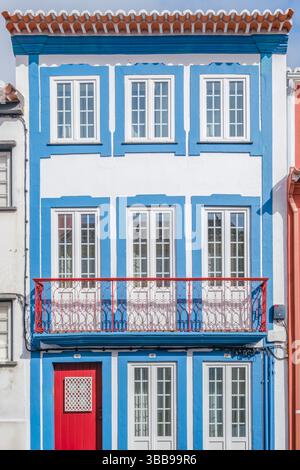 Farbenfrohe Gebäudefassade mit roter Tür und Balkon, Angra do Heroismo, Azoren. Bezaubernde Aussicht auf ein dreistöckiges Gebäude mit einer weiß-blauen Fassade, A Stockfoto