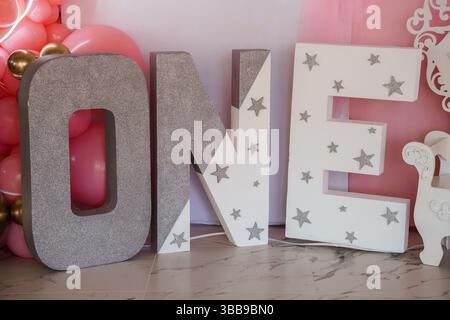 Eine glamouröse Kulisse für den ersten Geburtstag mit großen, glitzernden silbernen EINBUCHSTABEN, die mit Sternen verziert sind, sowie einem pastellrosa B Stockfoto