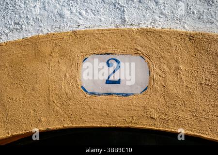 Keramikfliesen Haus Nummer zwei auf strukturierter Wand. Nahaufnahme einer dekorativen Keramikfliese mit der blauen Zahl „2“ mit blauem Rand, in eine te gesetzt Stockfoto
