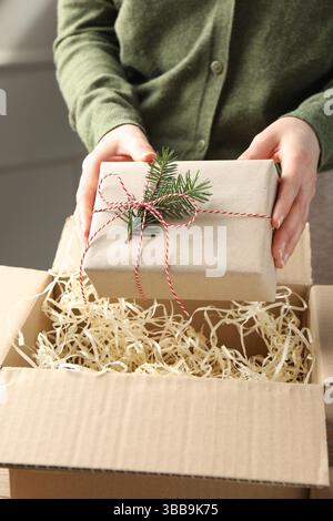 Frau packt Geschenk in Paketbox am Tisch, Nahaufnahme Stockfoto