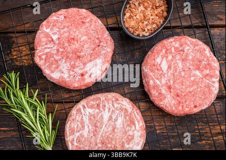 Gefrorene Fleischpasteten, bereit zum Grillen, Forcemeat von Schwein und Rindfleisch für Burger. Hölzerner Hintergrund. Draufsicht Stockfoto