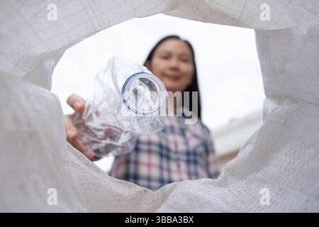 Eine asiatische Frau sortiert eine Plastikwasserflasche, die in den Müll gelegt wird, um sie für das Recycling zu sortieren, wirft verschiedene Arten von Flaschen in einen Müllbeutel. Stockfoto