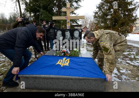 Männer setzten ukrainische Flagge auf das Grab der Helden der Kruty Kandyba Familie, Blumen. Die Schlacht bei Kruty fand 1918 statt, als ukrainische Kadetten die Rote Armee stoppten. Stockfoto