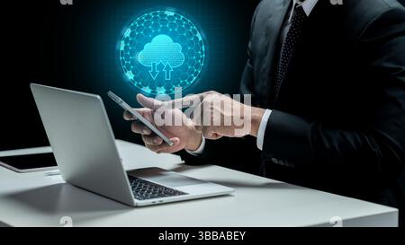 Geschäftsmann berührt Handy mit Cloud-Computing-Symbol. Laptop und Tablet auf dem Schreibtisch. Technologische Innovation auf dem virtuellen Bildschirm. Konzept eines DAT Stockfoto