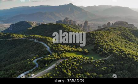 Blick aus der Vogelperspektive auf grüne Hügel und Felsformationen in Meteora, Griechenland, bei Sonnenuntergang in warmem, goldenem Licht. Stockfoto