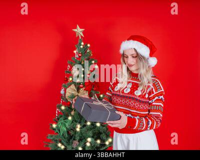 Blondes europäisches Mädchen, das allein Weihnachten feiert. Geschenkbox Geschenkbogenschleife halten. Sie sieht hübsch aus, lächelnd, positiv, glückliche Frau überrert. Stockfoto
