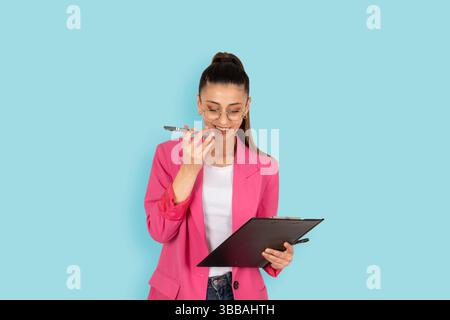 Geschäftsfrau mit Klemmbrett. Modische langhaarige Brünette, die am Telefon spricht. Technologie, Mode, Lifestyle-Konzept für Menschen. Isoliert blau Stockfoto
