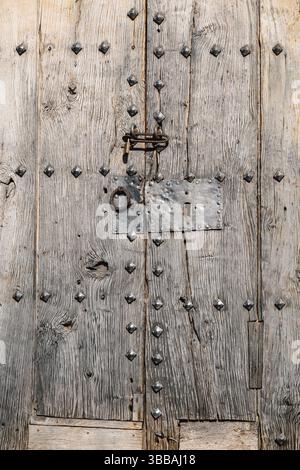 Verwitterte mittelalterliche Holztür mit Eisenstollen in einem alten Steinbogen. Historischer Eingang mit traditioneller Beschläge und gemauertem Mauerwerk-Featur Stockfoto