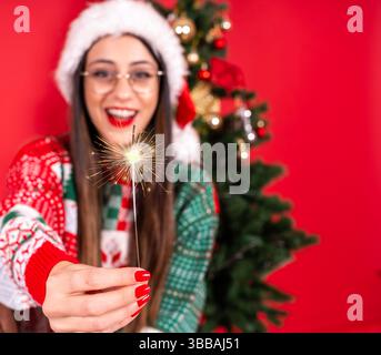 Fröhliches neues Jahr Party-Konzept, funkelnde oder bengalische Lichter brennen in der Hand, Nahaufnahme Bild einer Frau lächelnd aufgeregt tragen santa-Hut, Strickpullover. Stockfoto