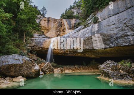 Geheime Wasserfalloase unter massivem Kalksteinüberhang. Kristallklares smaragdgrüner Wasser bildet ein natürliches Schwimmloch in einer höhlenähnlichen Umgebung Stockfoto