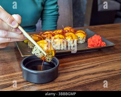 Handgebackene Sushi Roll in Sojasauce im japanischen Restaurant eintauchen. Nahaufnahme: Japanisches gebackenes Sushi mit Sojasauce und Ingwer genießen. Stockfoto