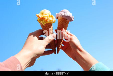 Zwei Hände halten zwei Eiskegel auf blauem Himmel. Konzept von Freundschaft, Freude, Glück Stockfoto