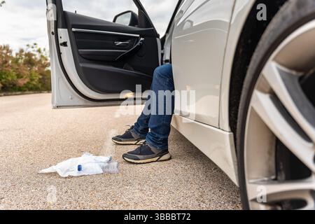 Ein Mann, der in seinem Auto sitzt und Müll auf die Straße wirft und die Umwelt verschmutzt. Stockfoto