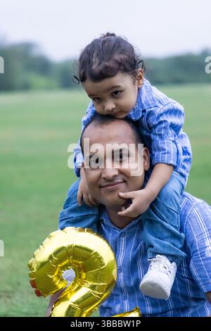 Sohn sitzt am Vater schulterbindende Momente am zweiten Geburtstag im Freien morgens Stockfoto