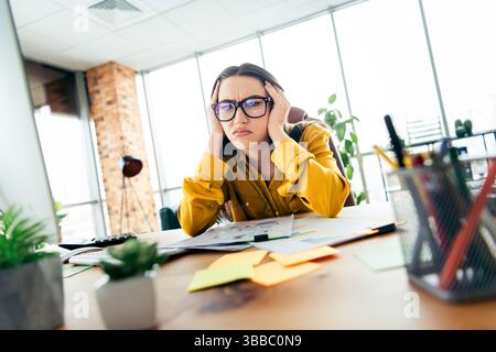 Die junge Geschäftsfrau frustrierte an ihrem Arbeitsplatz in einem modernen Bürobereich und kämpfte mit Aufgaben und Fristen Stockfoto